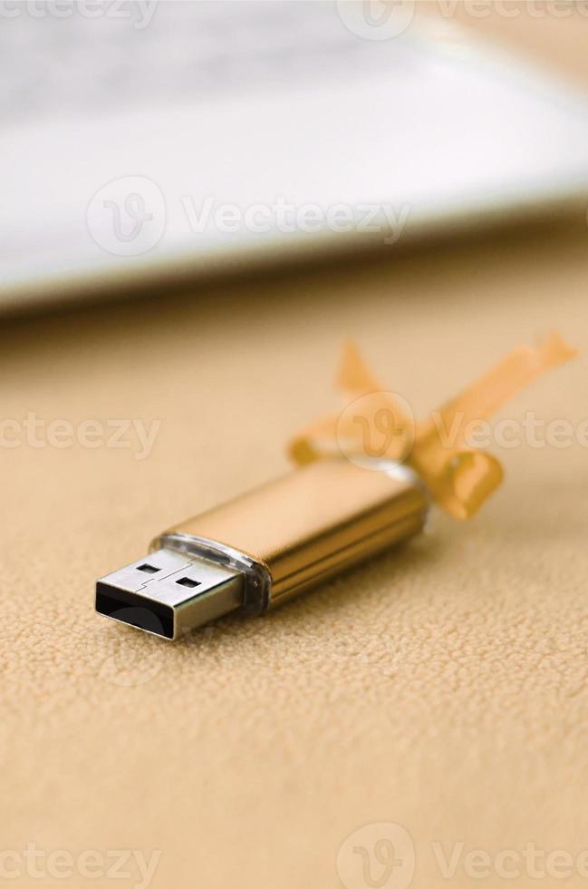 Orange usb flash memory card with a bow lies on a blanket of soft and furry light orange fleece fabric beside to a white laptop. Classic female gift design for a memory card photo