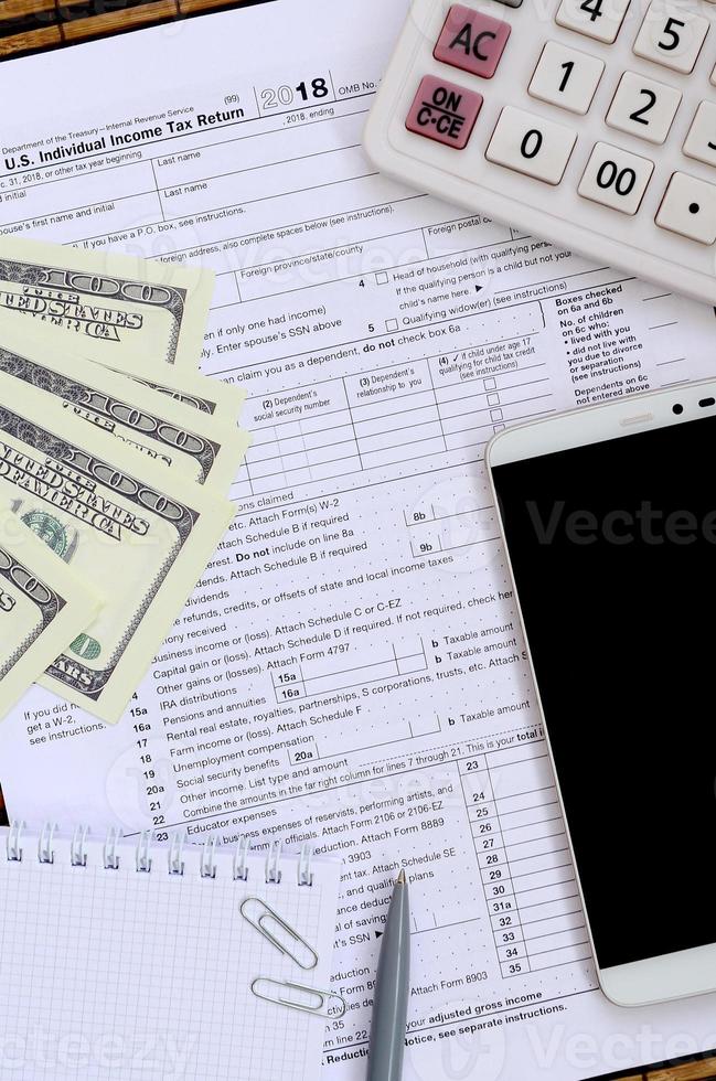 Composition of items lying on the 1040 tax form. Dollar bills, pen, calculator, smartphone, paper clip and notepad. The time to pay taxes photo