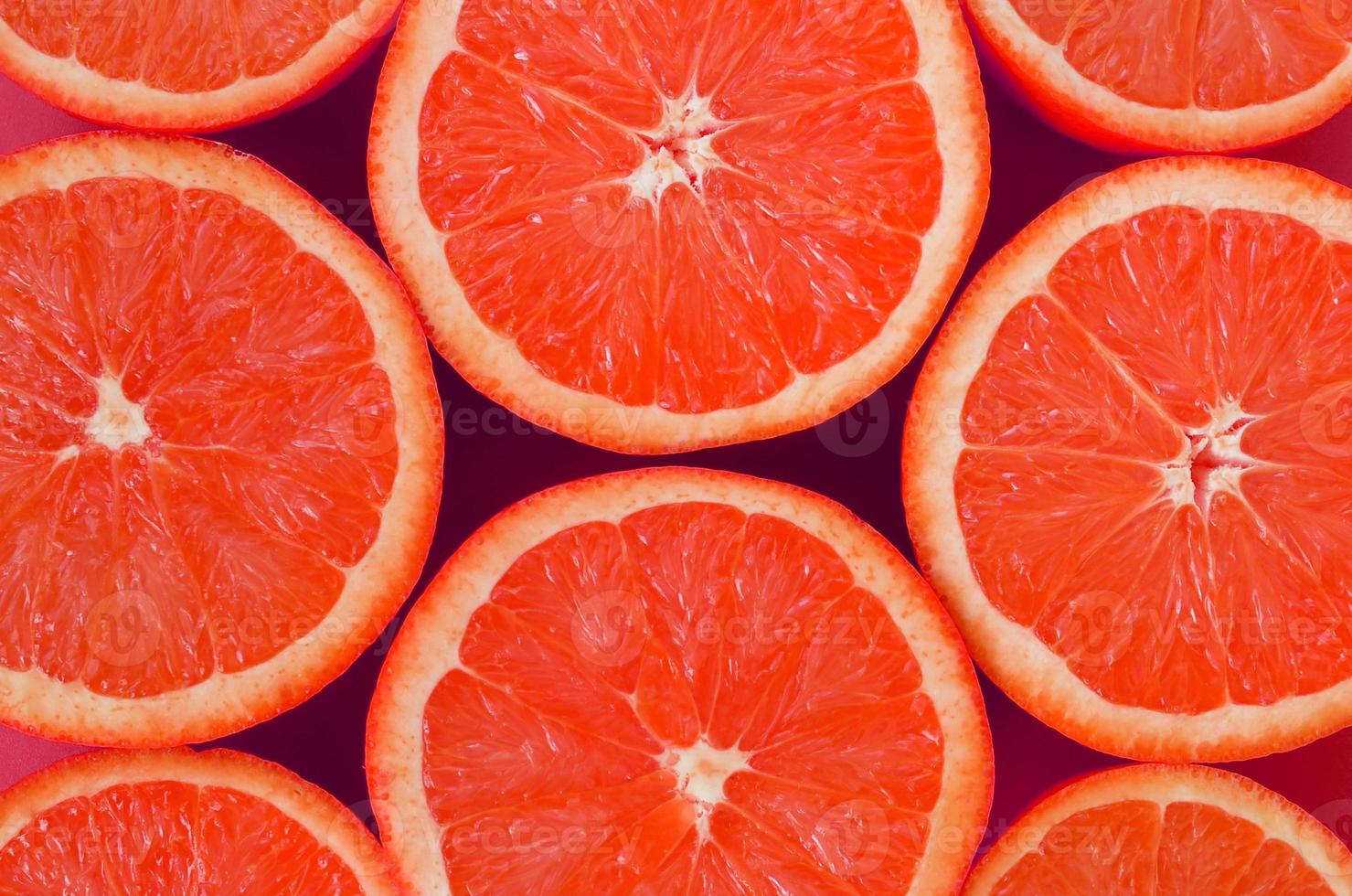 Top view of a several grapefruit slices on bright background in pink color. A saturated citrus texture image photo