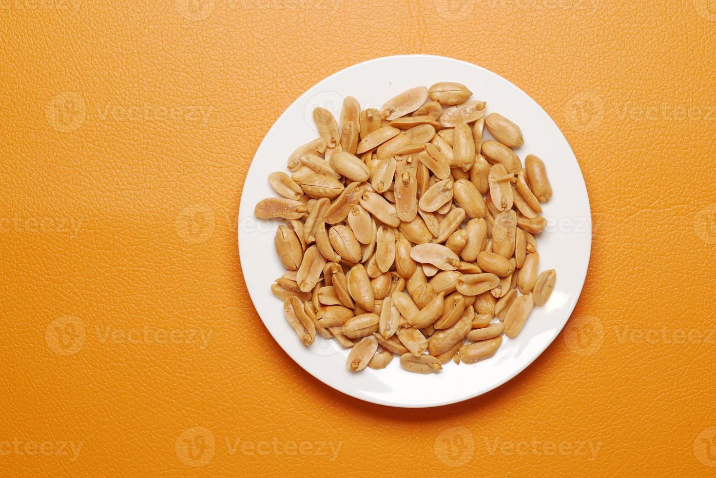 Peeled peanuts on a plate on orange background photo