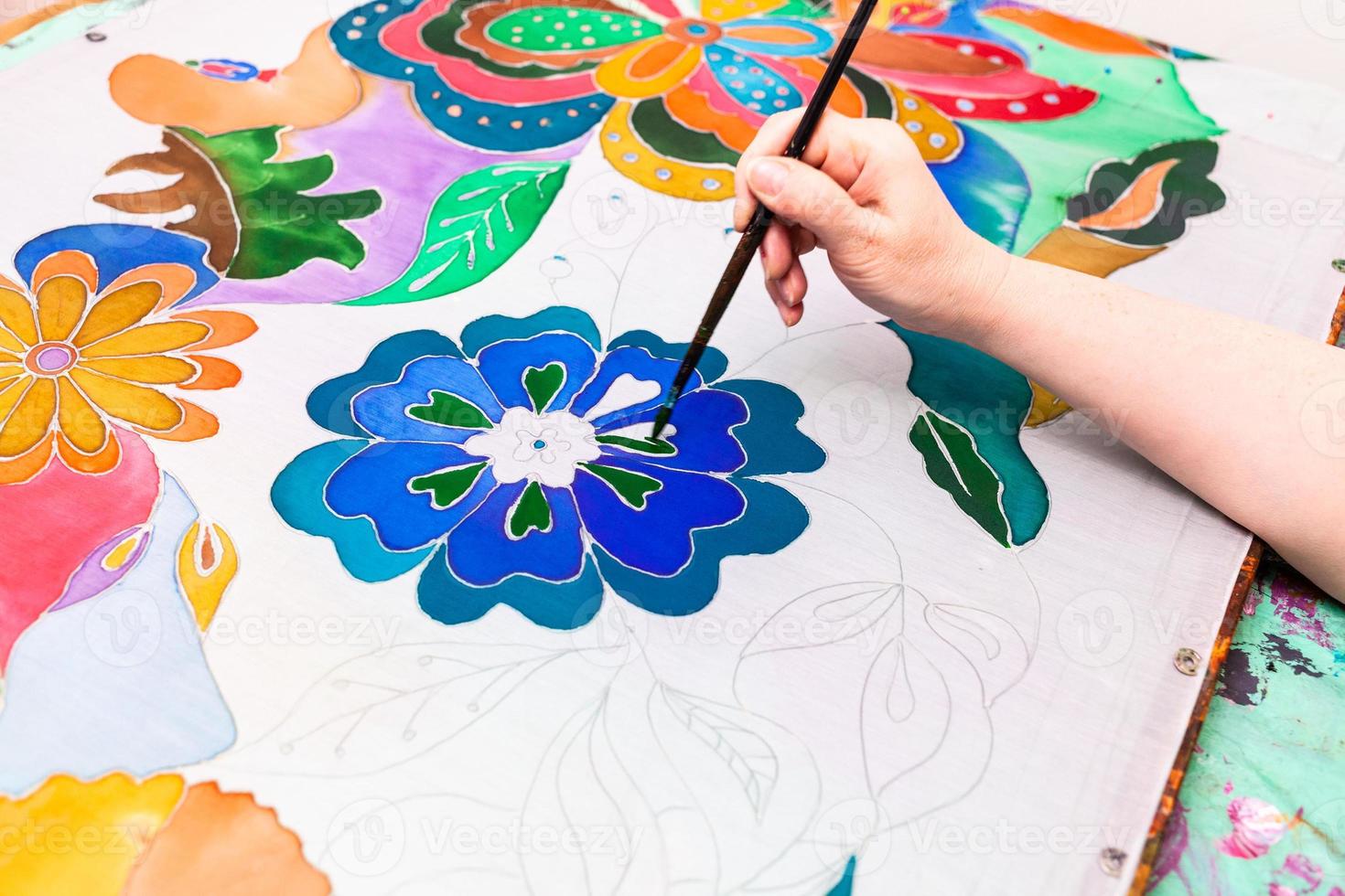 craftsman paints batik with floral pattern on silk photo