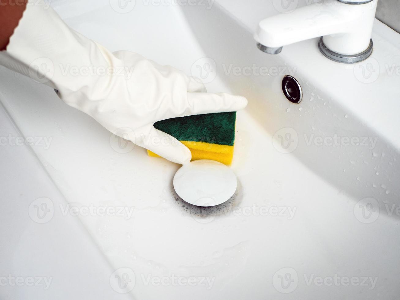 a hand in a white rubber glove with a sponge washes drain in the sink in the bathroom photo