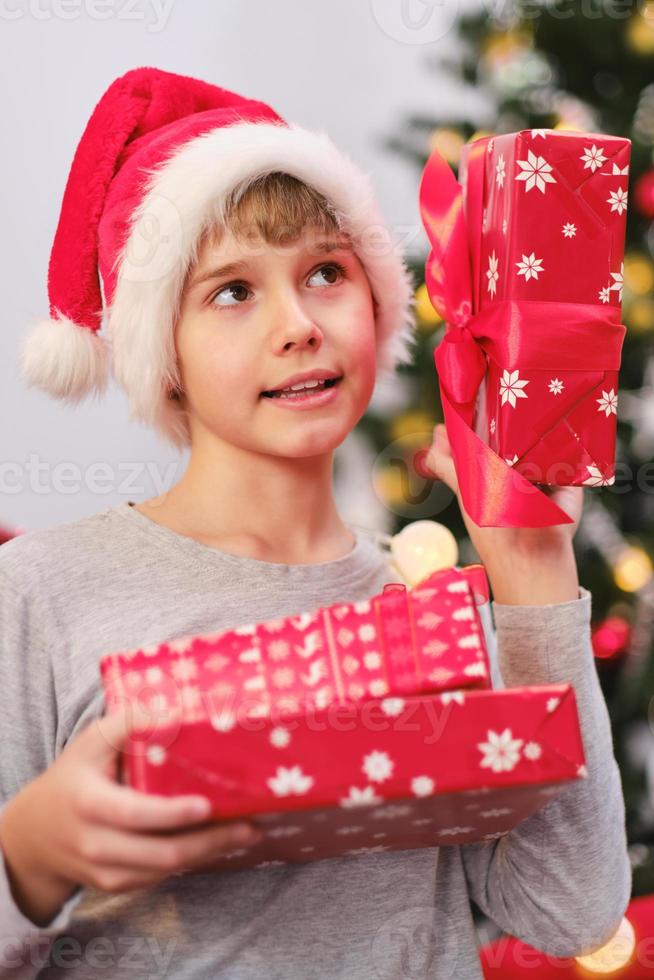 Portrait of a curious child holding presents by the Christmas tree on Christmas morning. photo