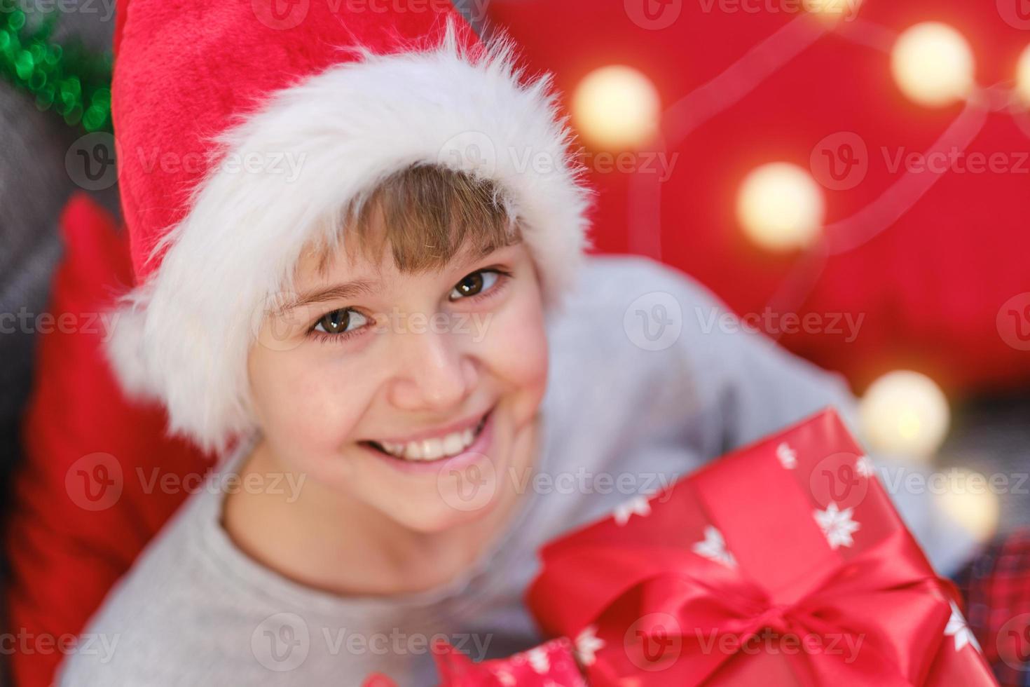 Portrait of a Christmas child in a Santa Claus hat with a Christmas present in his hands photo