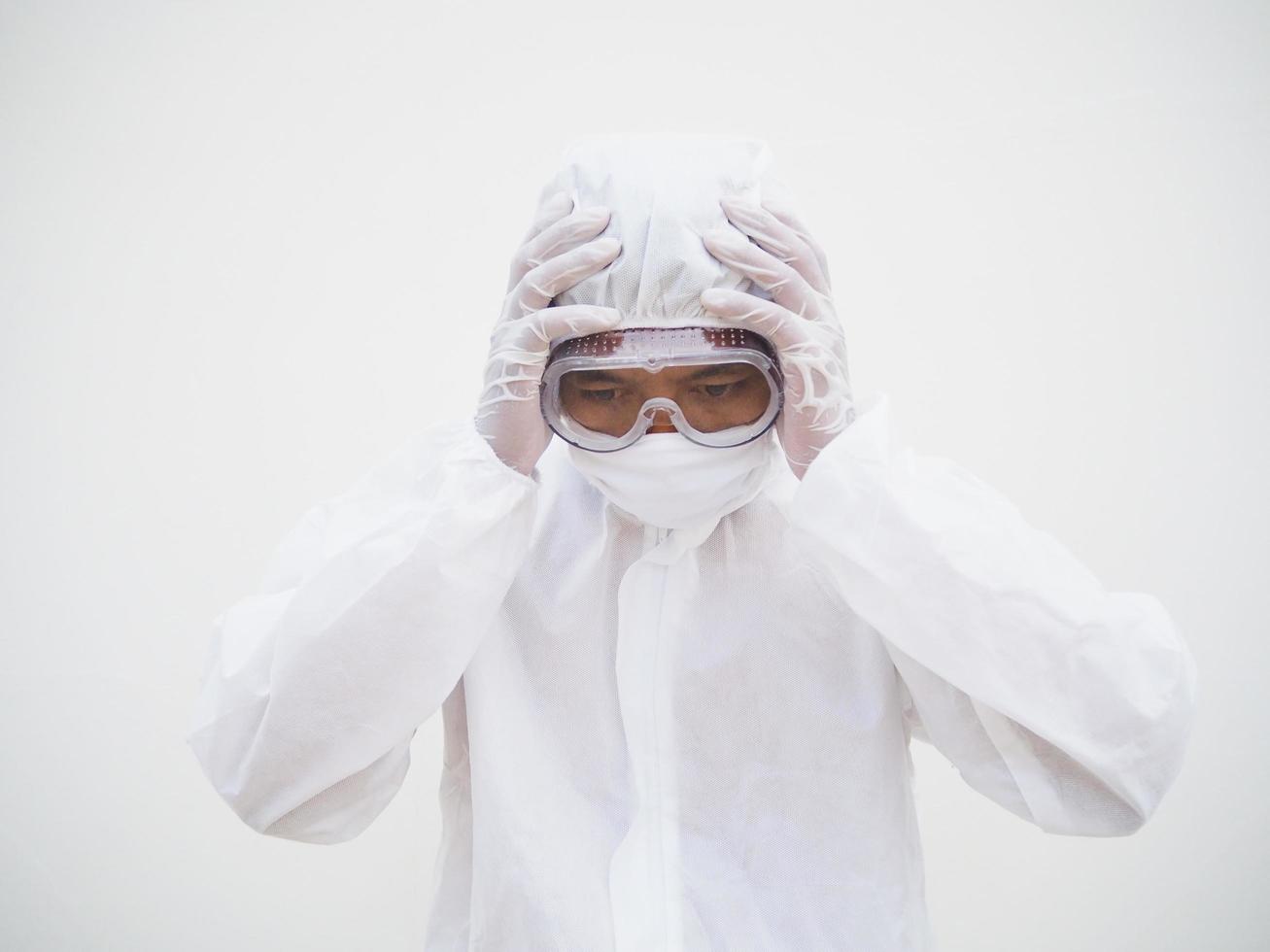 médico o científico masculino asiático con uniforme de suite de ppe de una manera que pone su mano sobre su cabeza sintiendo estrés y dolor de cabeza. concepto de coronavirus o covid-19 fondo blanco aislado foto