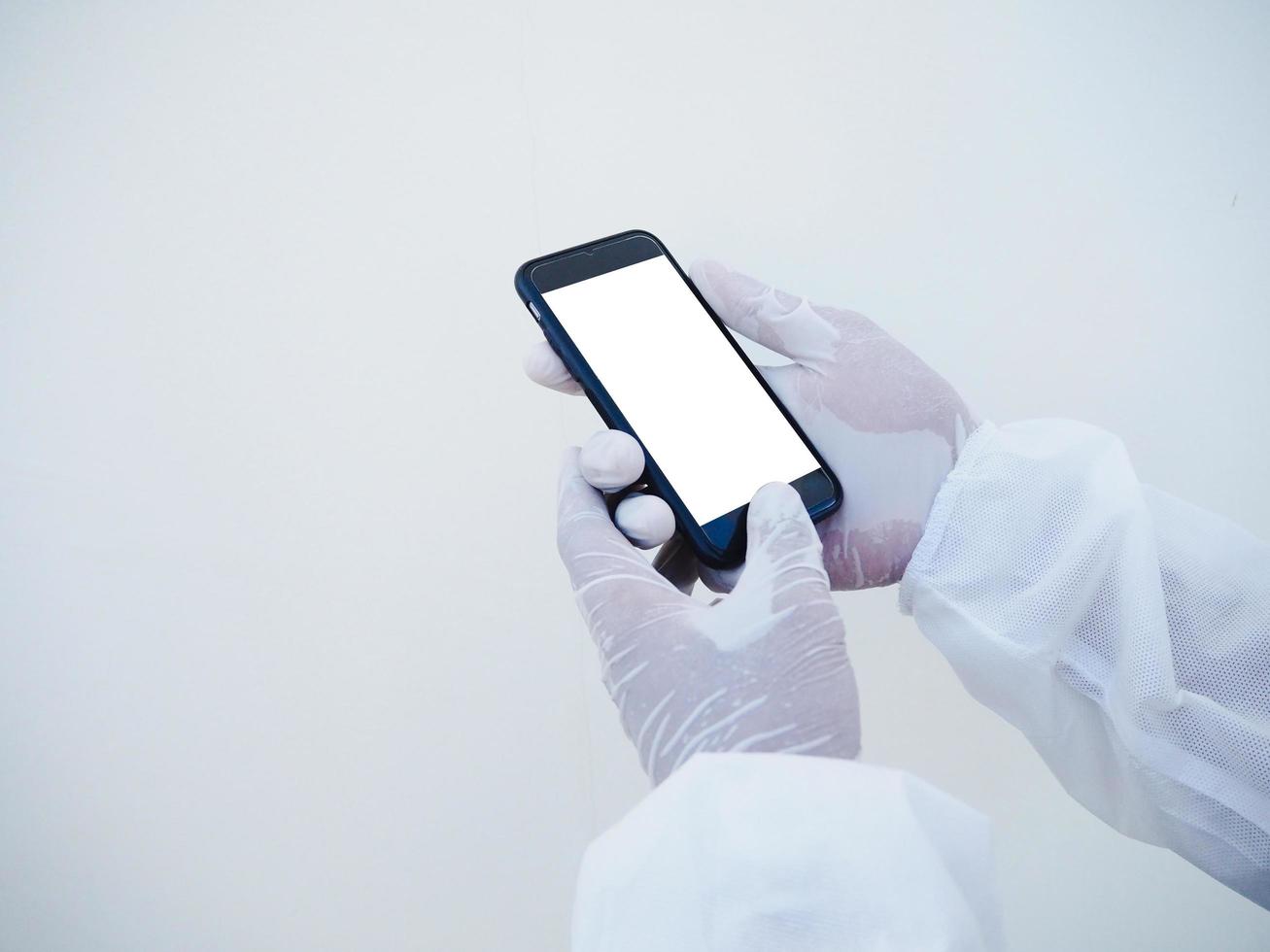 cerrar las manos de un médico o científico con uniforme de suite de ppe sosteniendo un teléfono inteligente con pantalla blanca en blanco para texto o diseño. concepto de coronavirus o covid-19 fondo blanco aislado foto