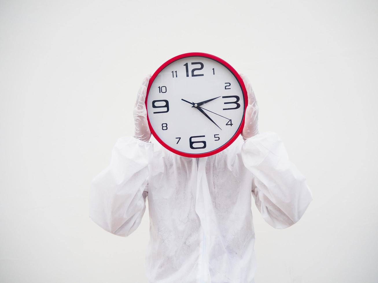 Portrait of doctor or scientist in PPE suite uniform holding red alarm clock and looking at the camera In various gestures. COVID-19 concept isolated white background photo