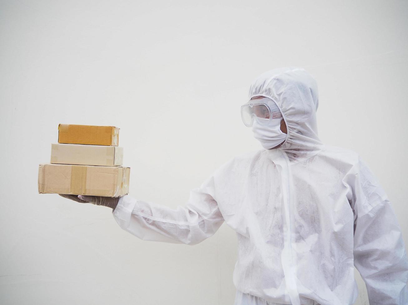 Young man in PPE suite uniform while holding cardboard boxes in medical rubber gloves and mask. coronavirus or COVID-19 concept isolated white background photo