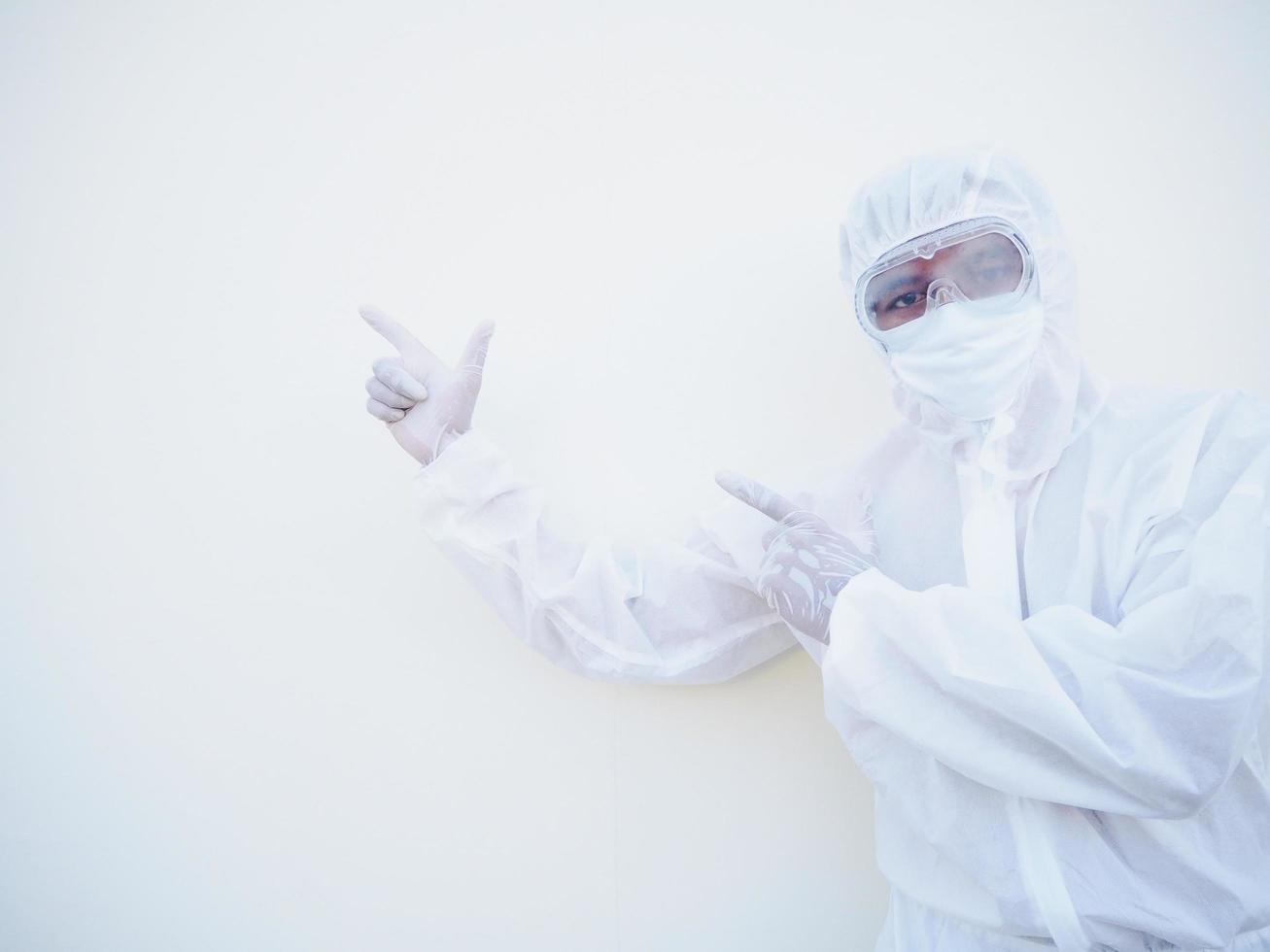 médico o científico masculino asiático con uniforme de suite de ppe que muestra señalar con dos dedos el espacio de la copia mientras está de pie y mirando hacia adelante. concepto de coronavirus o covid-19 fondo blanco aislado foto