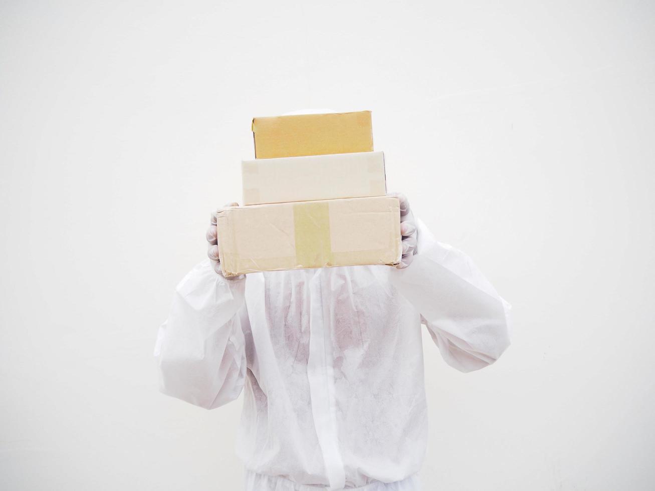 Young man in PPE suite uniform while holding cardboard boxes in medical rubber gloves and mask. coronavirus or COVID-19 concept isolated white background photo