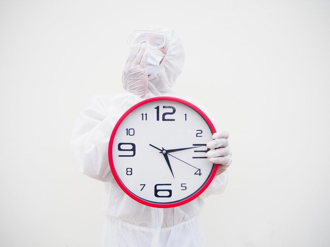 Portrait of doctor or scientist in PPE suite uniform holding red alarm clock and looking at the camera In various gestures. COVID-19 concept isolated white background photo