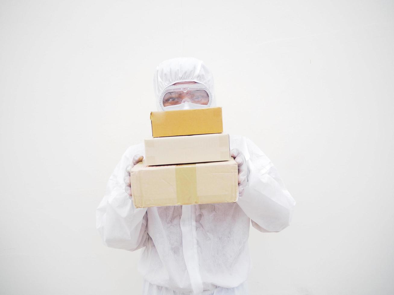 joven con uniforme de suite de ppe mientras sostiene cajas de cartón con guantes médicos de goma y máscara. concepto de coronavirus o covid-19 fondo blanco aislado foto