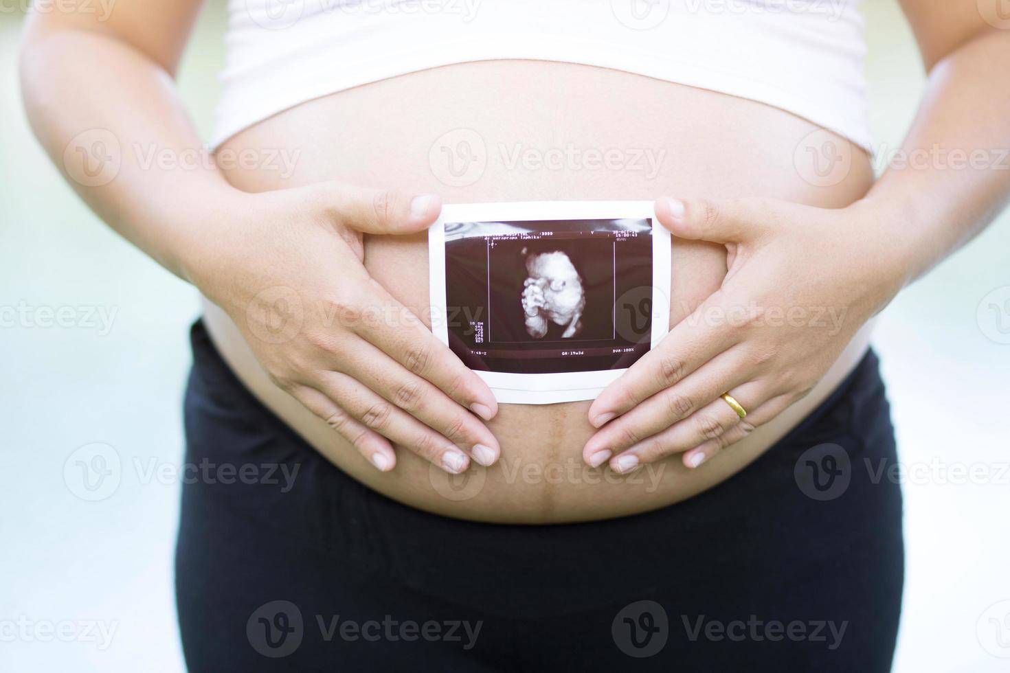 la mujer embarazada y su esposo empalman la mano abrazando la barriga en forma de corazón muestran amor por el bebé por nacer en el vientre relajándose en casa en el dormitorio. esperar la fecha de nacimiento esperando un puesto de bebé al aire libre foto