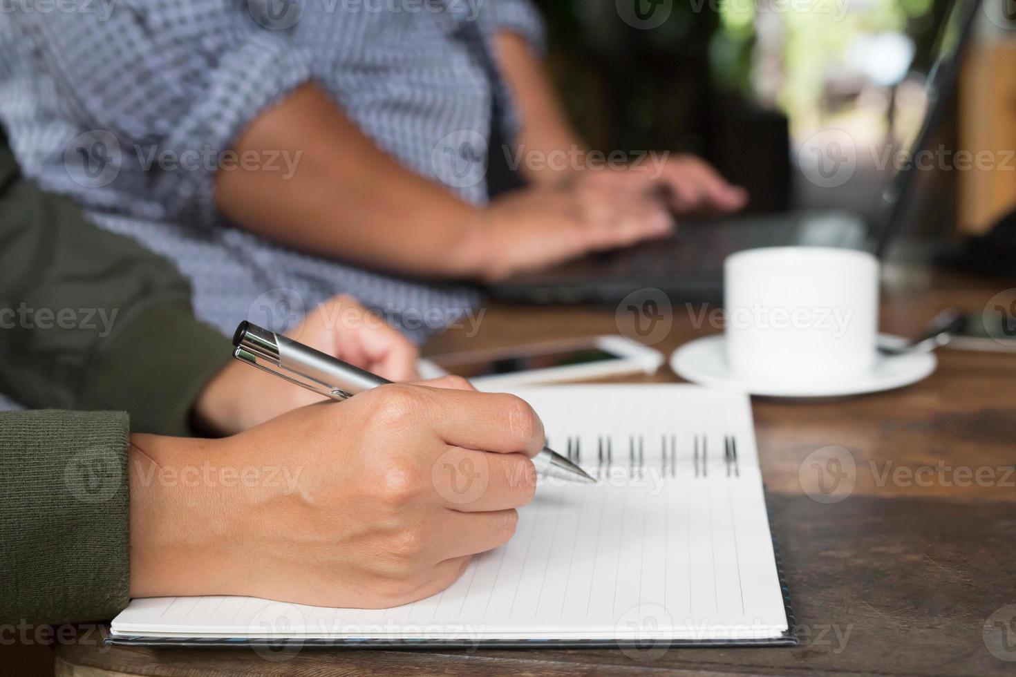 Woman freelancer working hand writing journal on small notebook notepad in coffee shop using with copy space area. photo