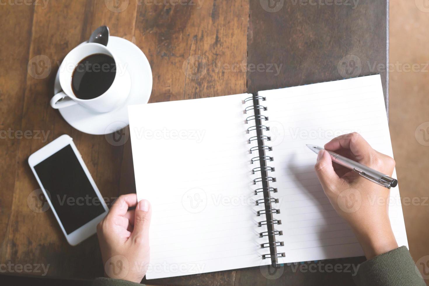 Woman freelancer working hand writing journal on small notebook notepad in coffee shop using with copy space area. photo