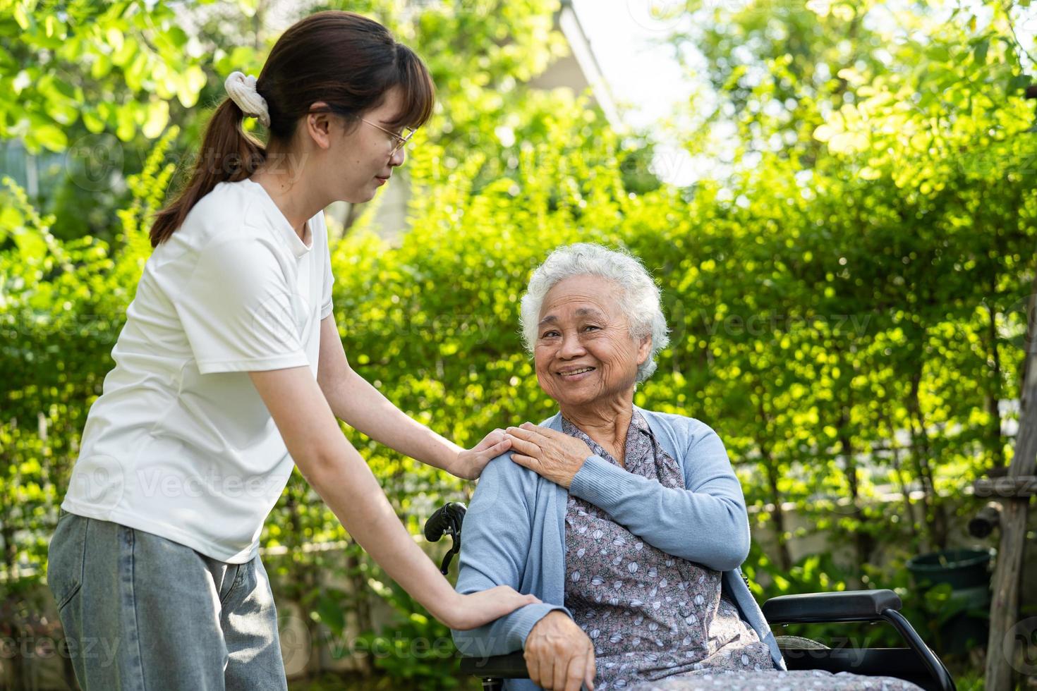 cuidador ayuda y cuida a una anciana asiática o anciana paciente sentada en silla de ruedas en el parque, concepto médico fuerte y saludable. foto