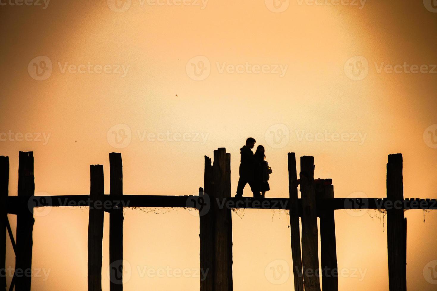 Silhouette of a couple walking on the U Bein Bridge with sunset twilight sky in background, Mandalay, Myanmar photo