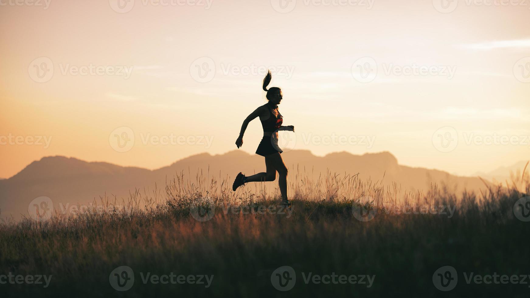 A young sportswoman runs at sunset in the hills photo