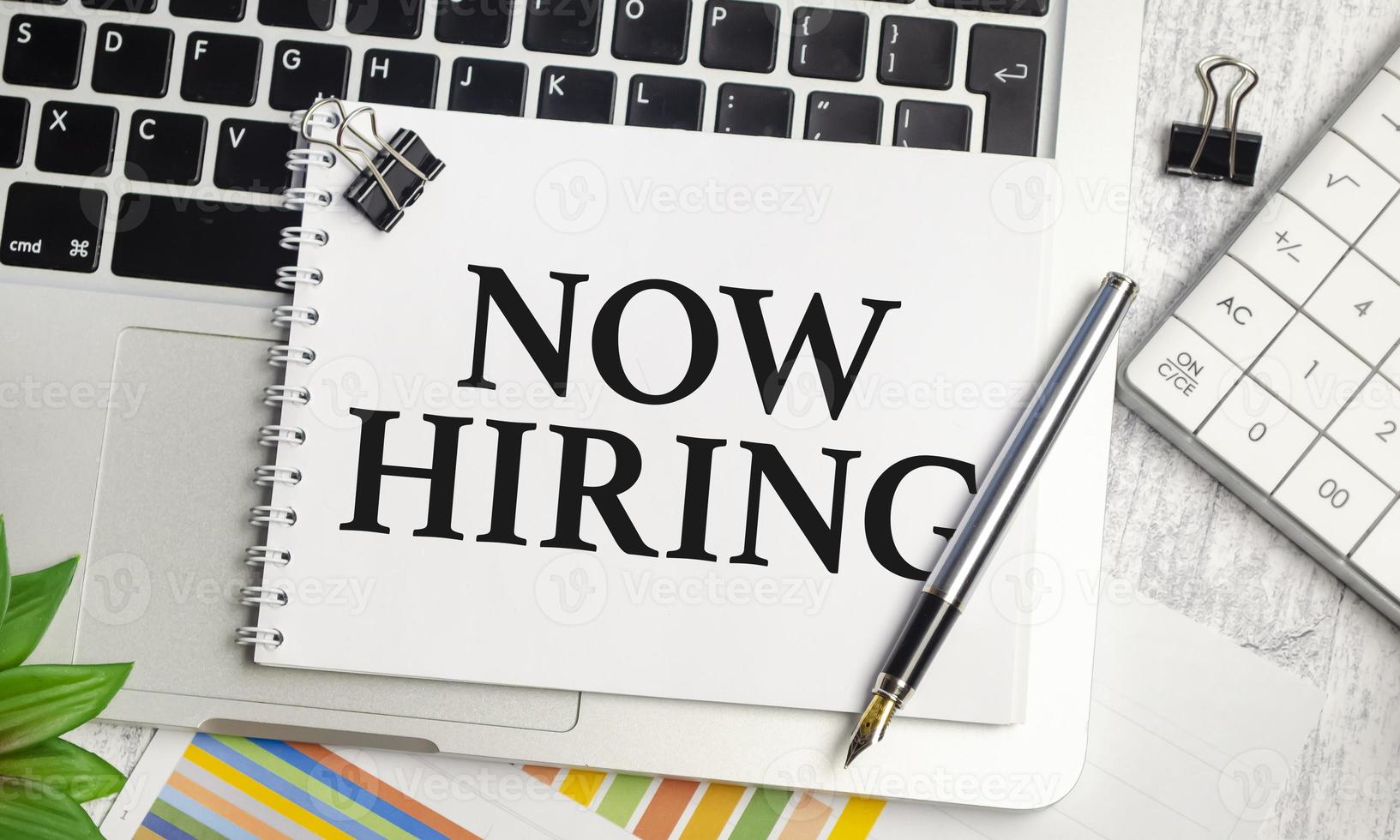 Now Hiring text and notepad with pen, charts and calculator photo