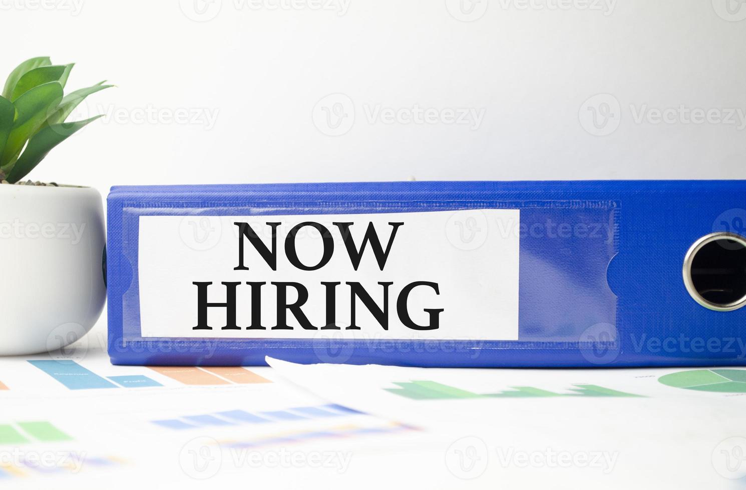 Now Hiring text written on blue folder and charts photo