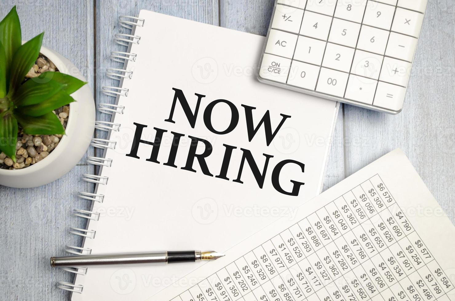 Now Hiring word on notepad with glasses and chart photo