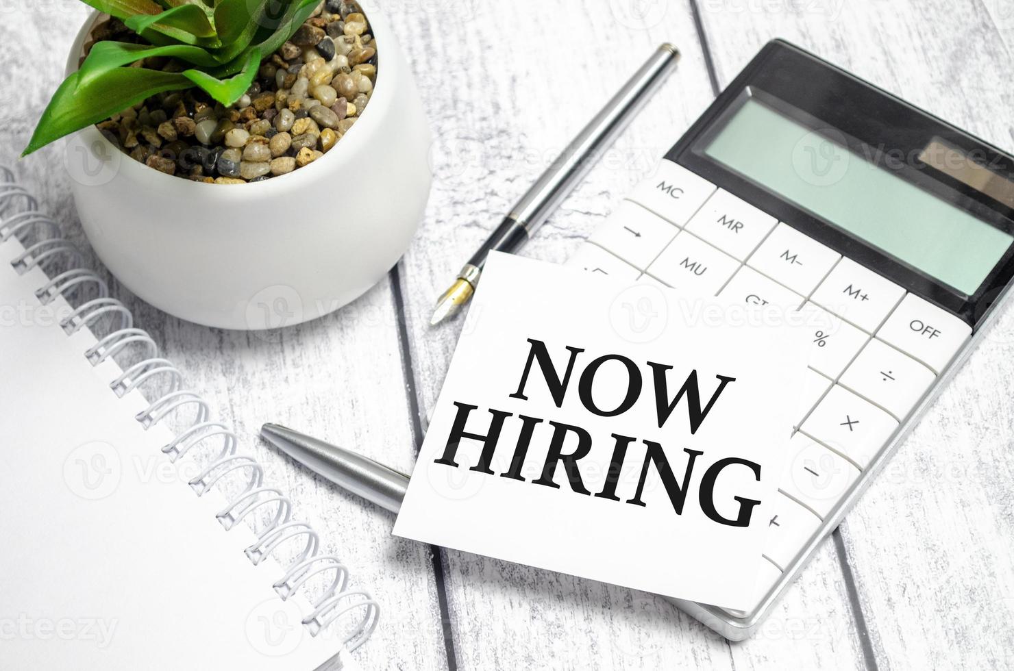 Now Hiring words on paper sticker and calculator on wooden background photo