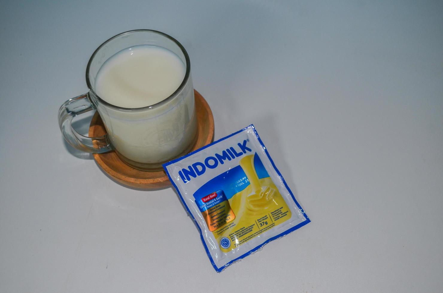 BLITAR, INDONESIA - October 3rd 2022 Top view Glass of white milk and Indomilk white creamer in sachet isolated on white background. Copy space object photo