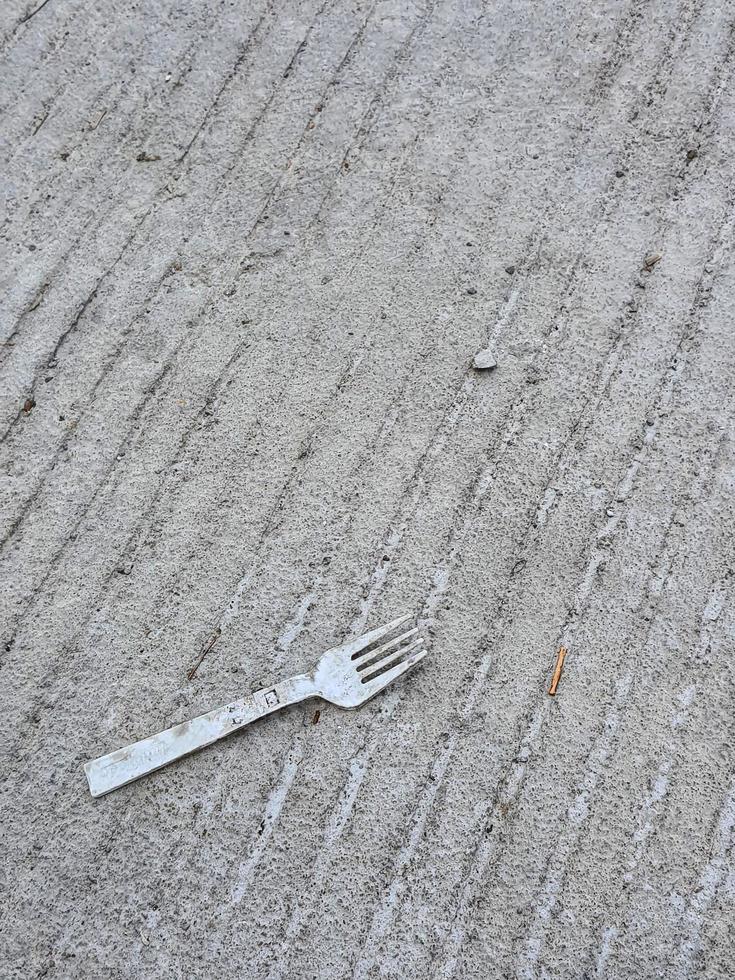 A plastic fork litter on top of a concrete road. Ab photo