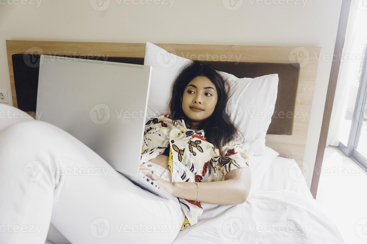 Serious concentrated young woman working from the bed. Hold the laptop on the knees and type on the keyboard. photo