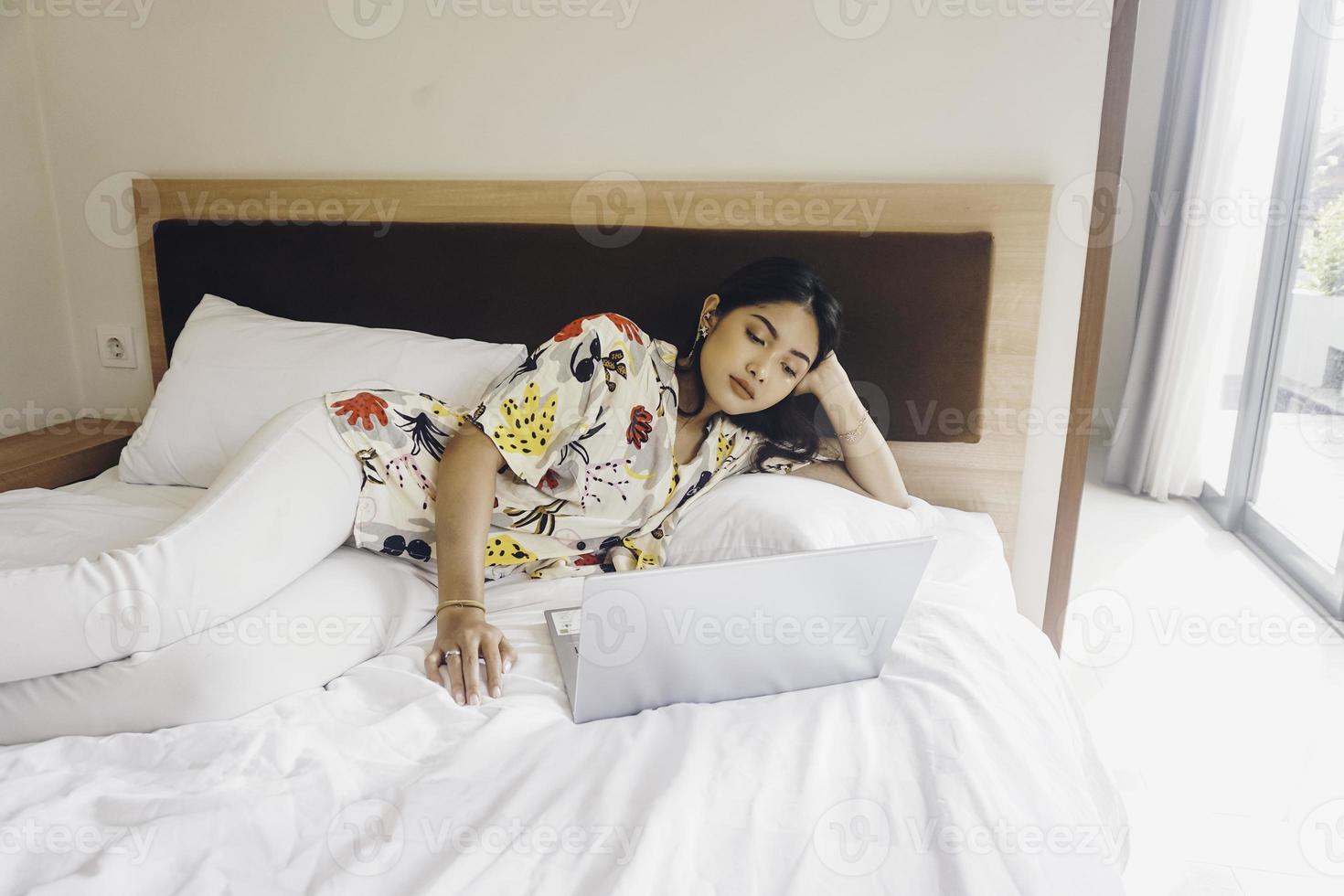 Serious concentrated young woman working from the bed. Hold the laptop on the knees and type on the keyboard. photo