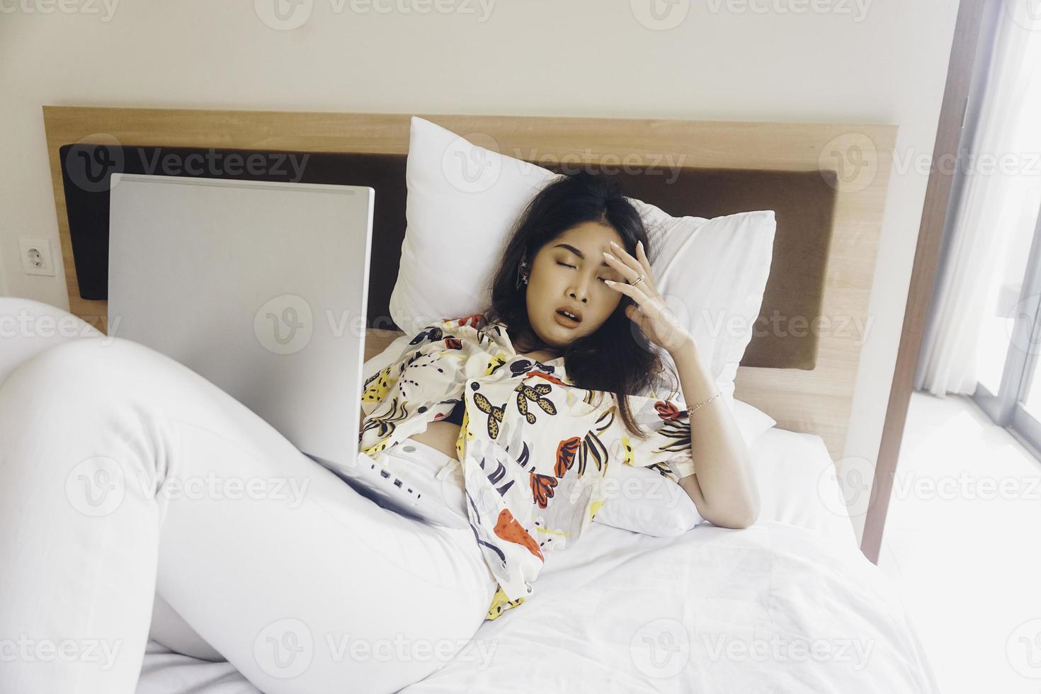 A sleepy young woman yawning while working from the bed. photo