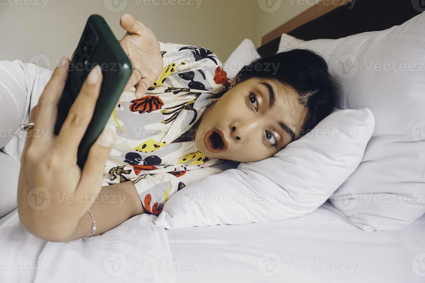 Shocked young woman checking on her phone while lying in bed photo