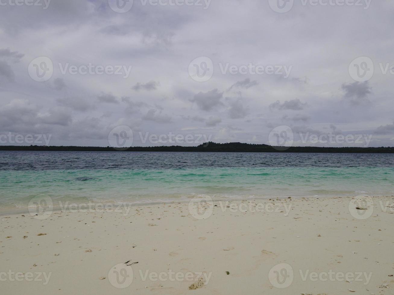 Beautiful sunny day on a calm pristine beach with grey skies in Indonesia photo