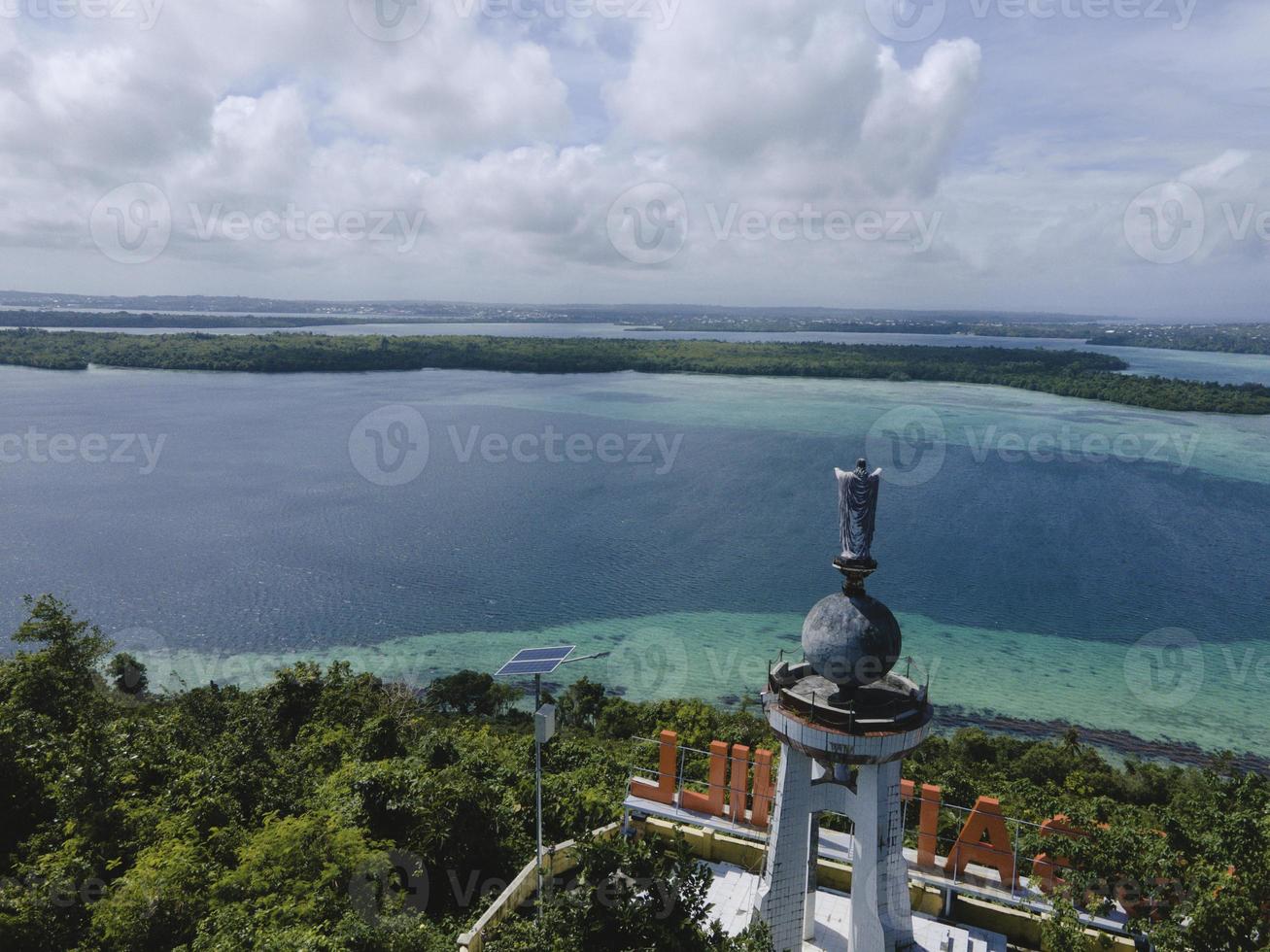 Aerial view of Jesus statue with beautiful beach view in small island. Maluku, Indonesia - July, 2022 photo