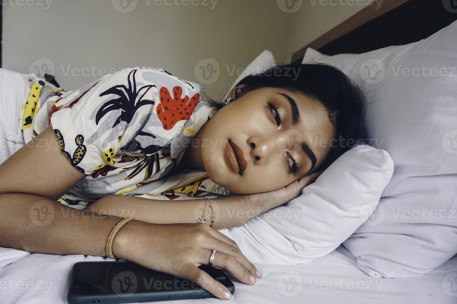 A young Asian woman on the bed feels sleepy, she is lying on the side and yawning photo