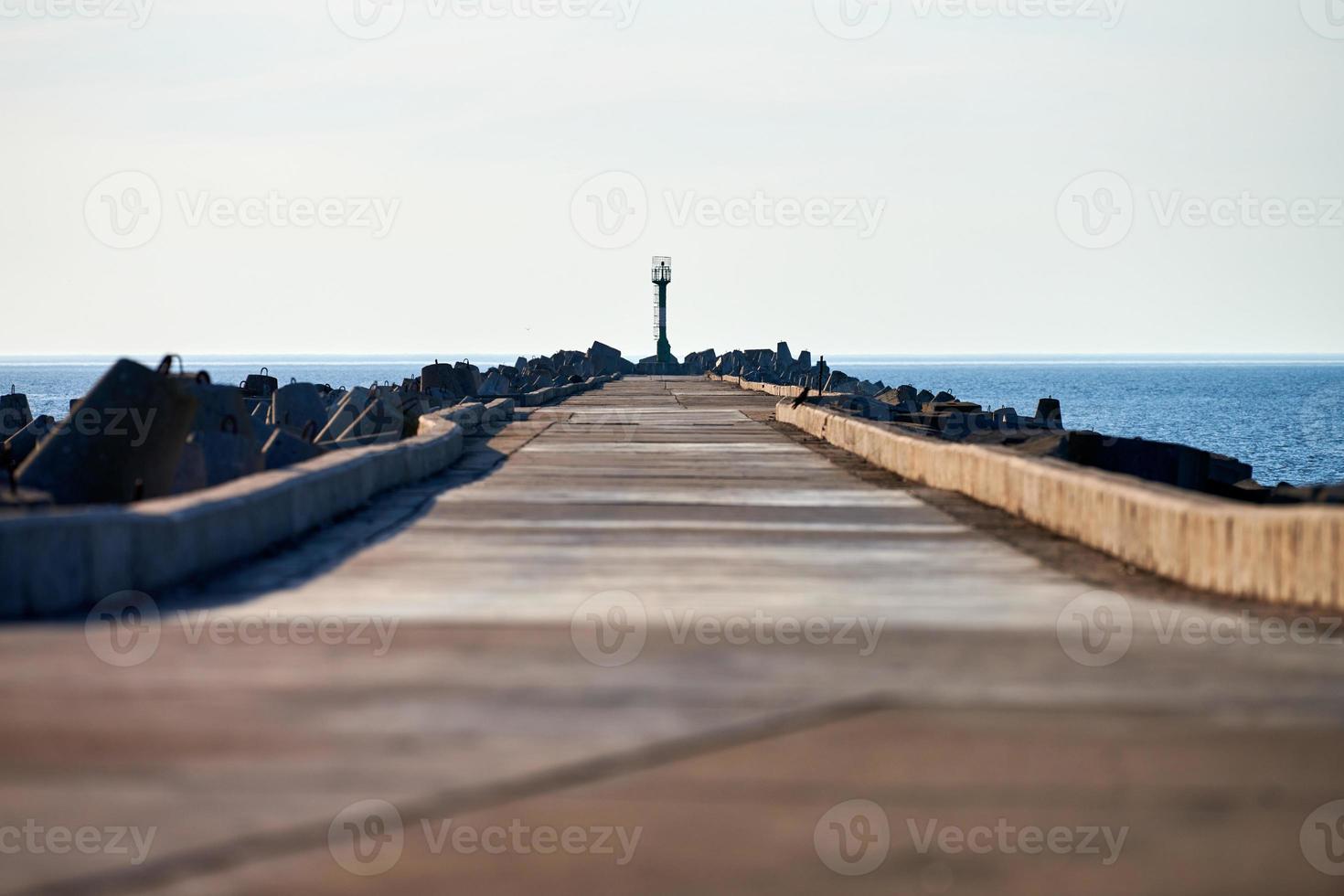 Empty long concrete pier with breakwaters and signal lighthouse in European port, copy space photo