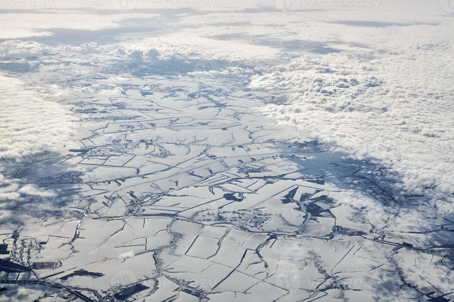 Aerial view over clouds top to snow covered rivers, fields and roads, winter fresh frosty air photo