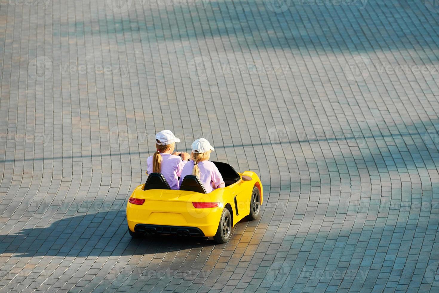 Two little girls driving toy car. Battery vehicle with remote control for children entertainment photo