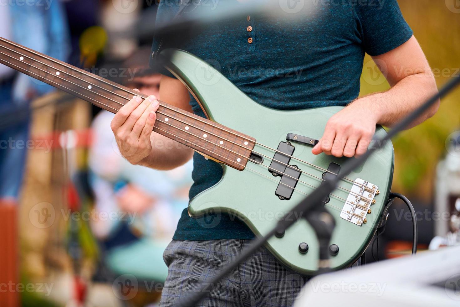 Hands of bassist playing green bass electric guitar on concert stage, musician playing bass guitar photo