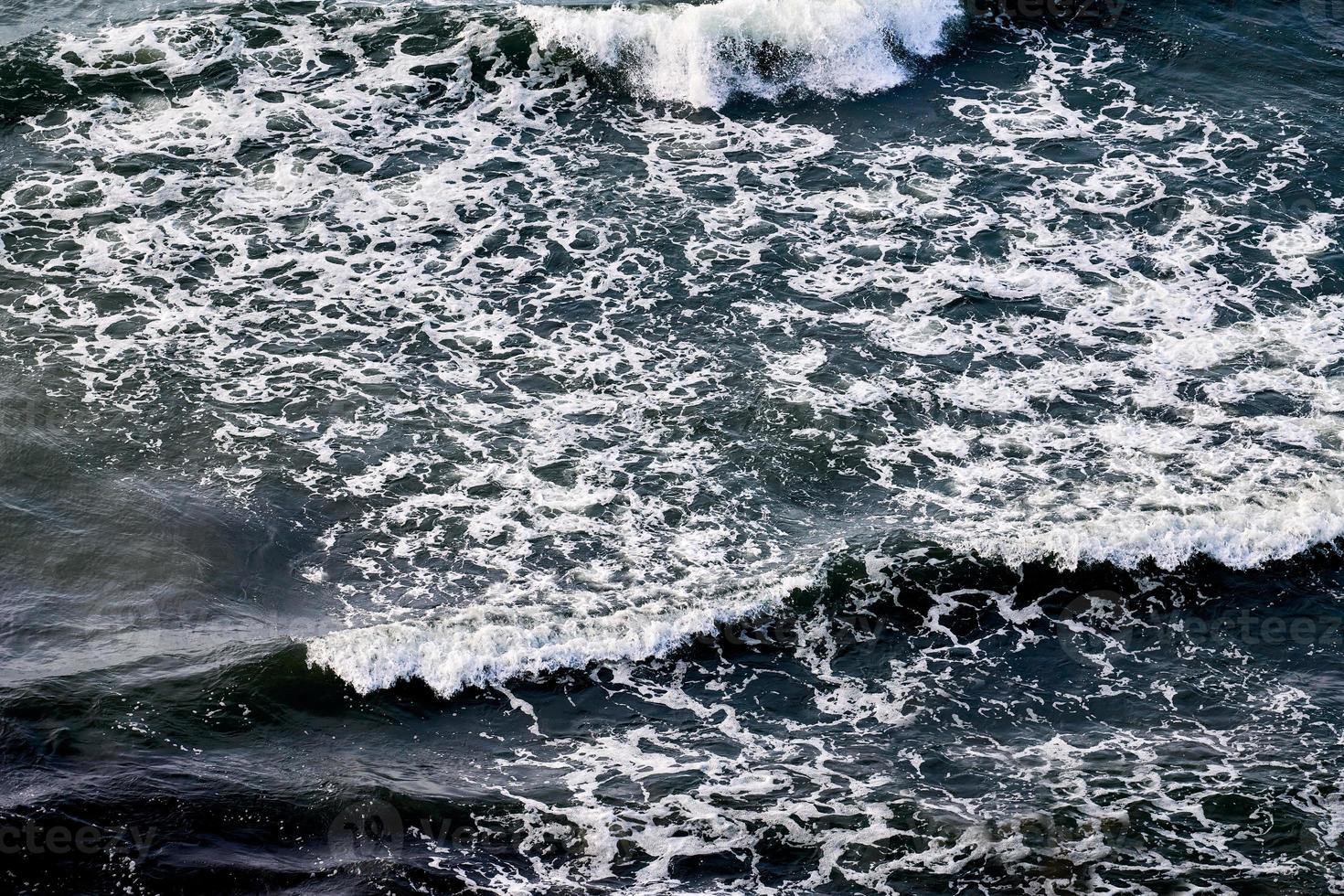 aguas de mar azul profundo salpicadas de olas espumosas, superficie de agua oceánica ondulada azul oscuro, rocío de mar foto