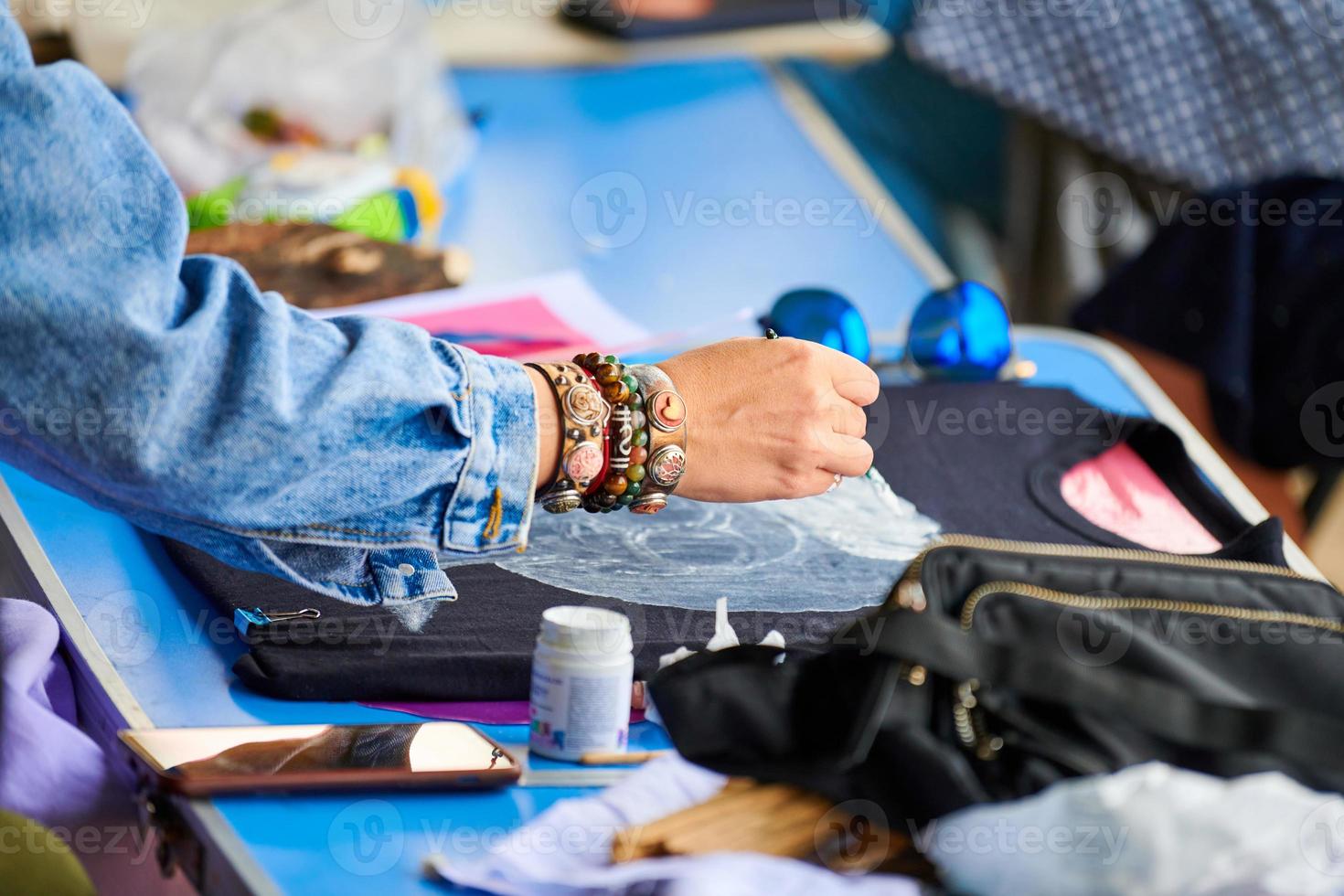 Woman painting abstract picture on black T-shirt using brush and fabric paint at workshop, handmade photo