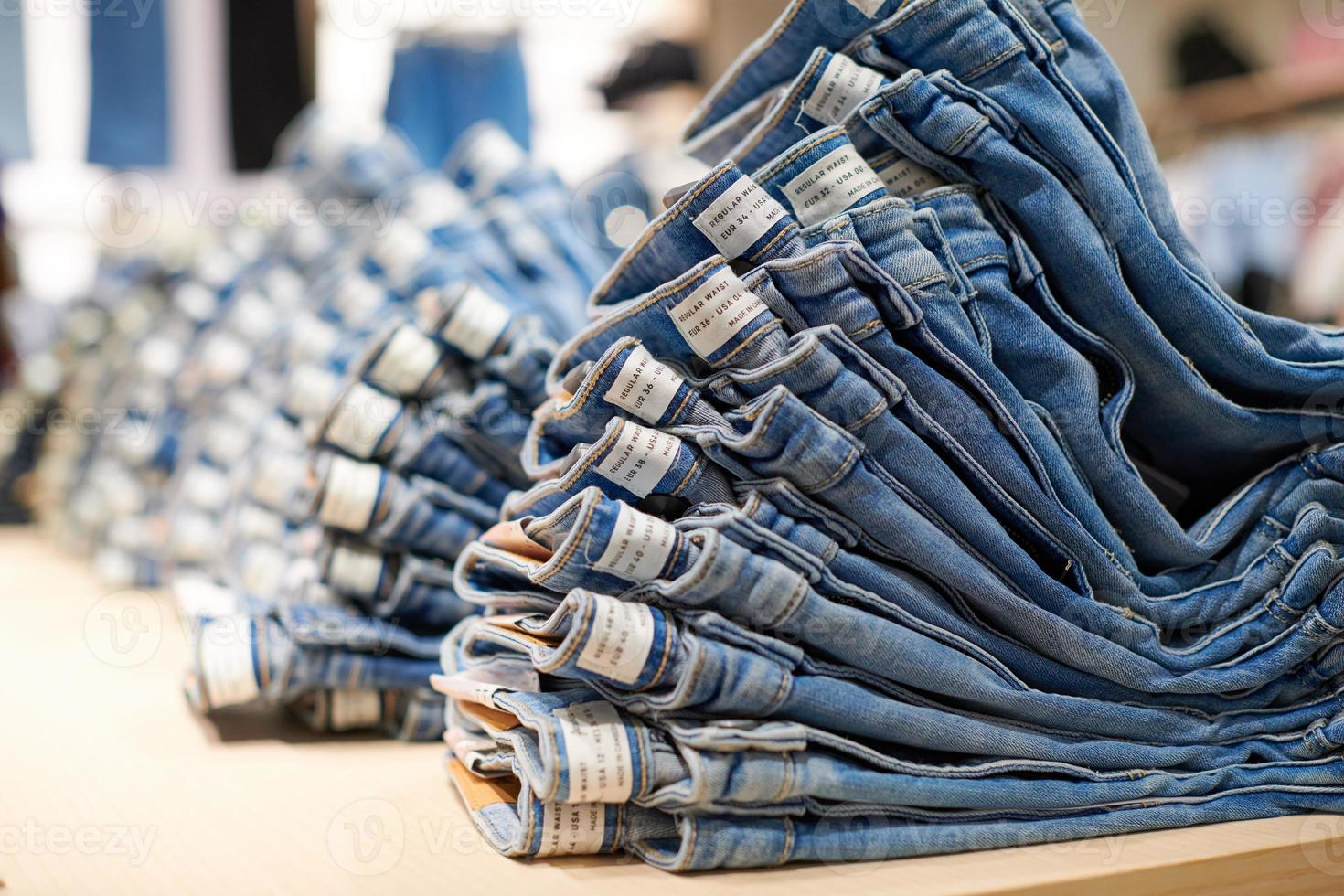 Denim jeans stack on wood table in clothing store, shopping photo