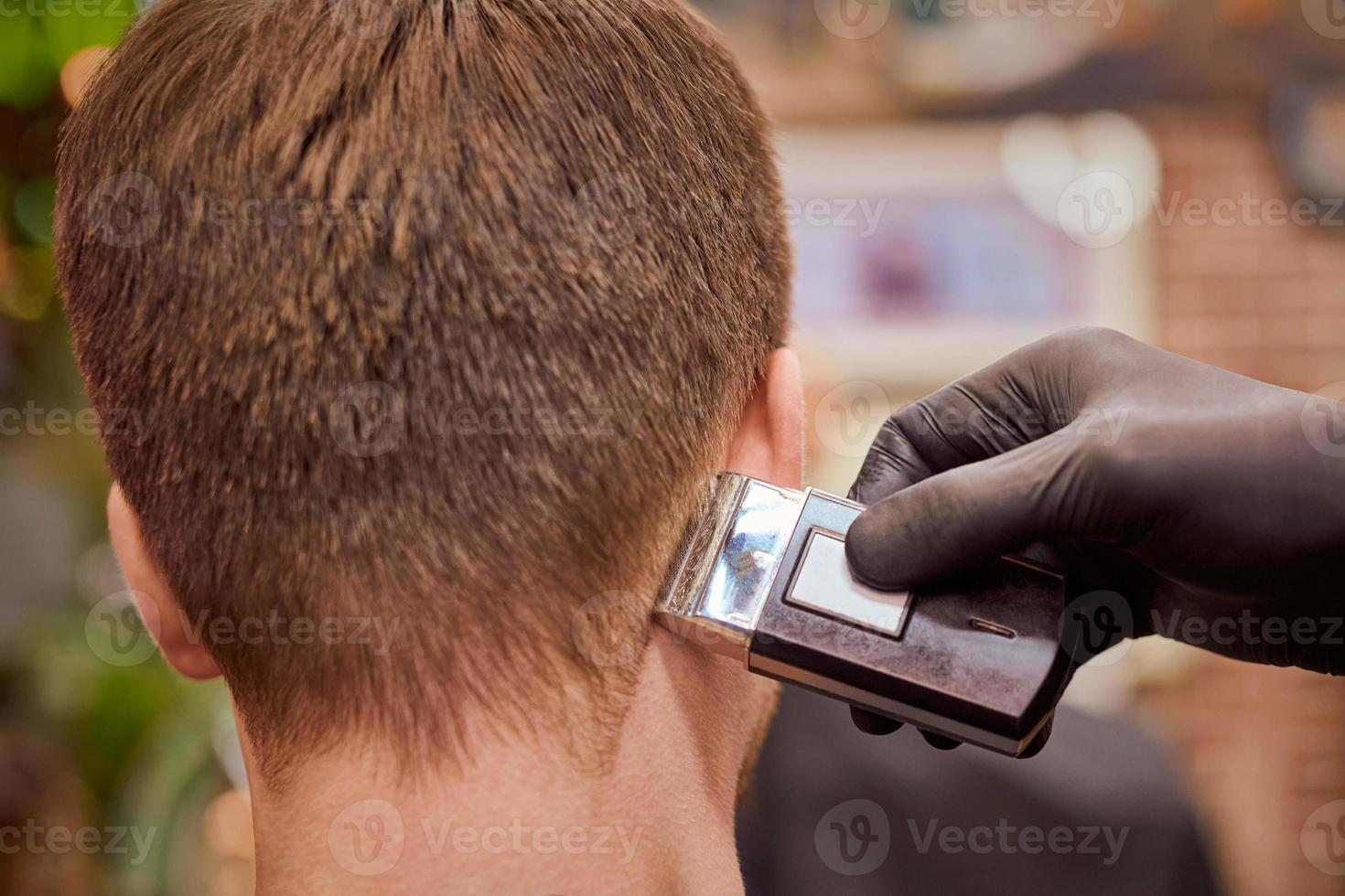 Male haircut shaving in barbershop, client getting haircut by hairdresser with electric shaver photo