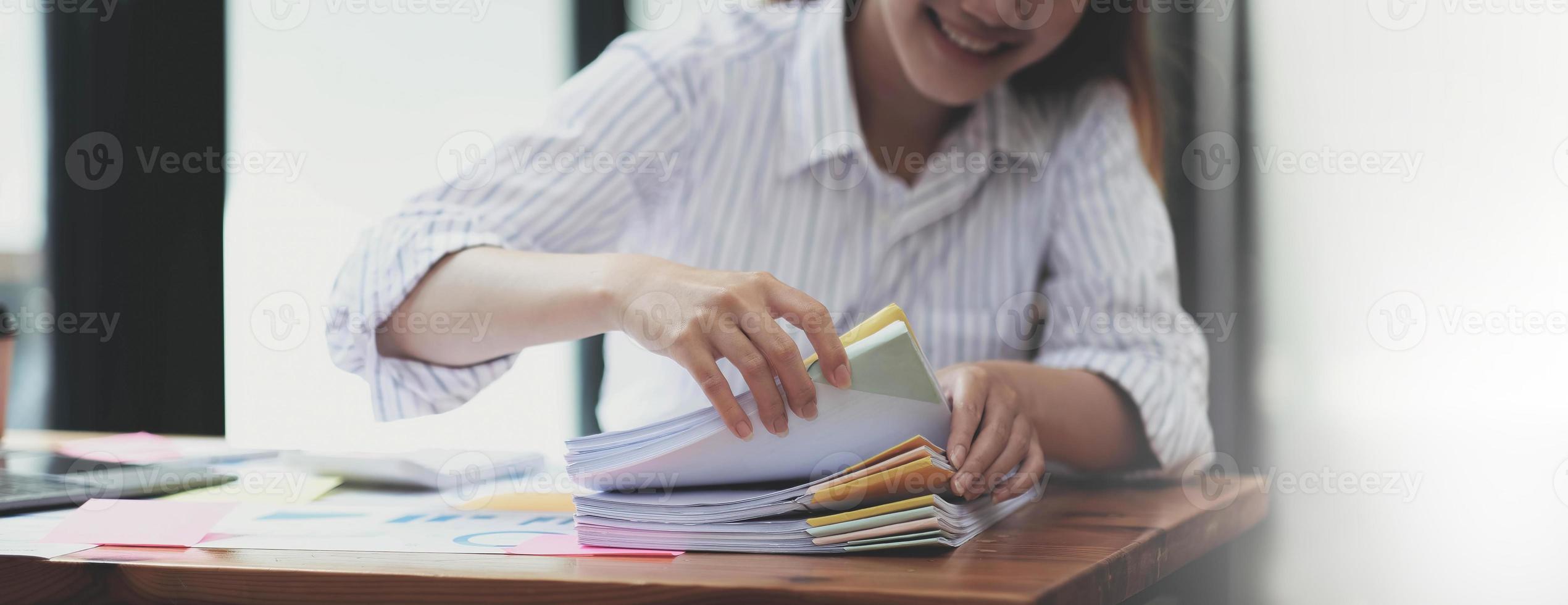 concepto de documentos comerciales manos de una mujer empleada trabajando en pilas de archivos en papel para buscar y verificar los logros de documentos inacabados en carpetas de papeles en una oficina de escritorio ocupada. enfoque suave foto