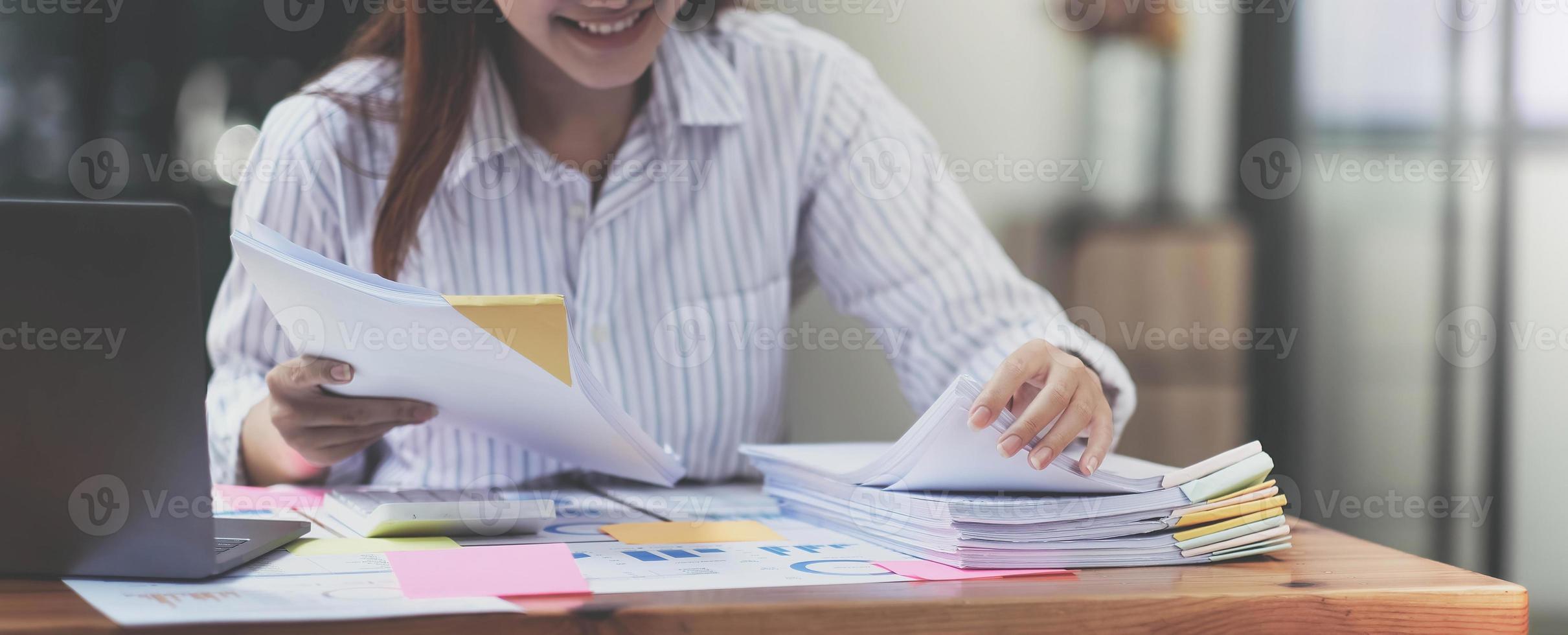 Business Documents concept  Employee woman hands working in Stacks paper files for searching and checking unfinished document achieves on folders papers at busy work desk office. Soft focus photo