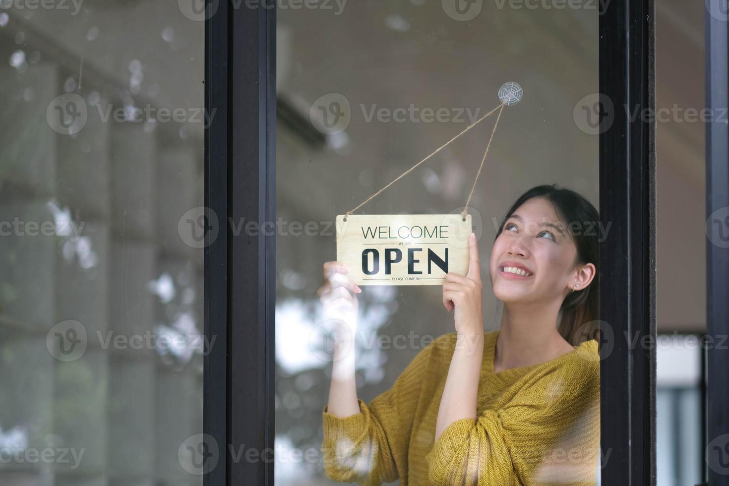 Small business owner smiling while turning the sign for the opening of the place after the quarantine due to covid-19. Close up of woman hands holding sign now we are open support local business. photo