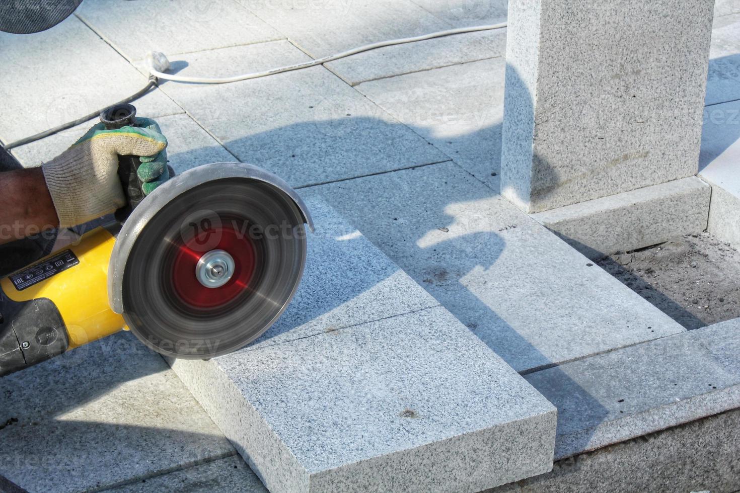 Hands of worker with electric grinder trims paving slabs on the construction site. Concept of laying new sidewalk tile. Stone cutting equipment. Road works. Civil engineering. Repair asphalt. Close-up photo