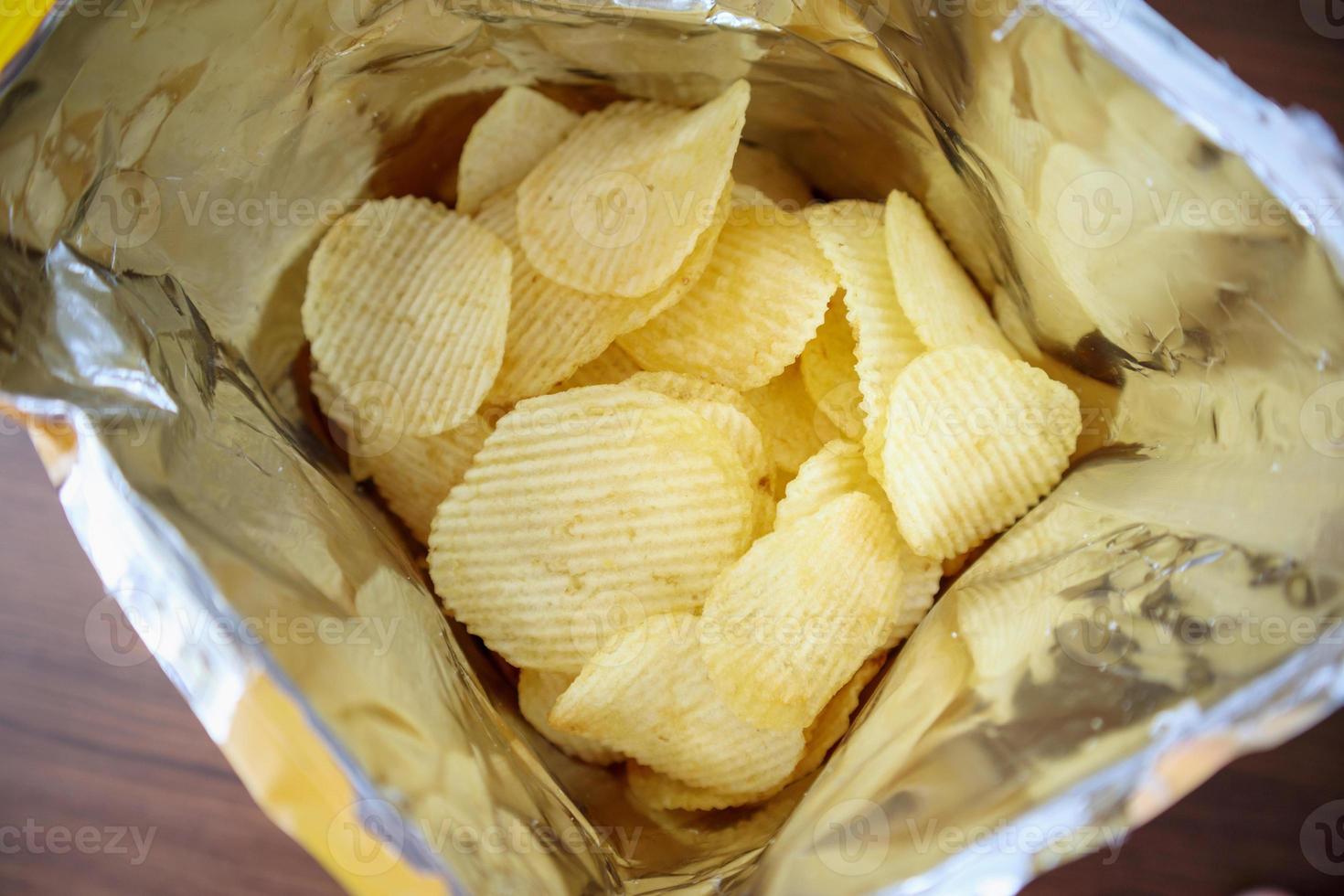 Potato chips in open snack bag close up on table floor photo
