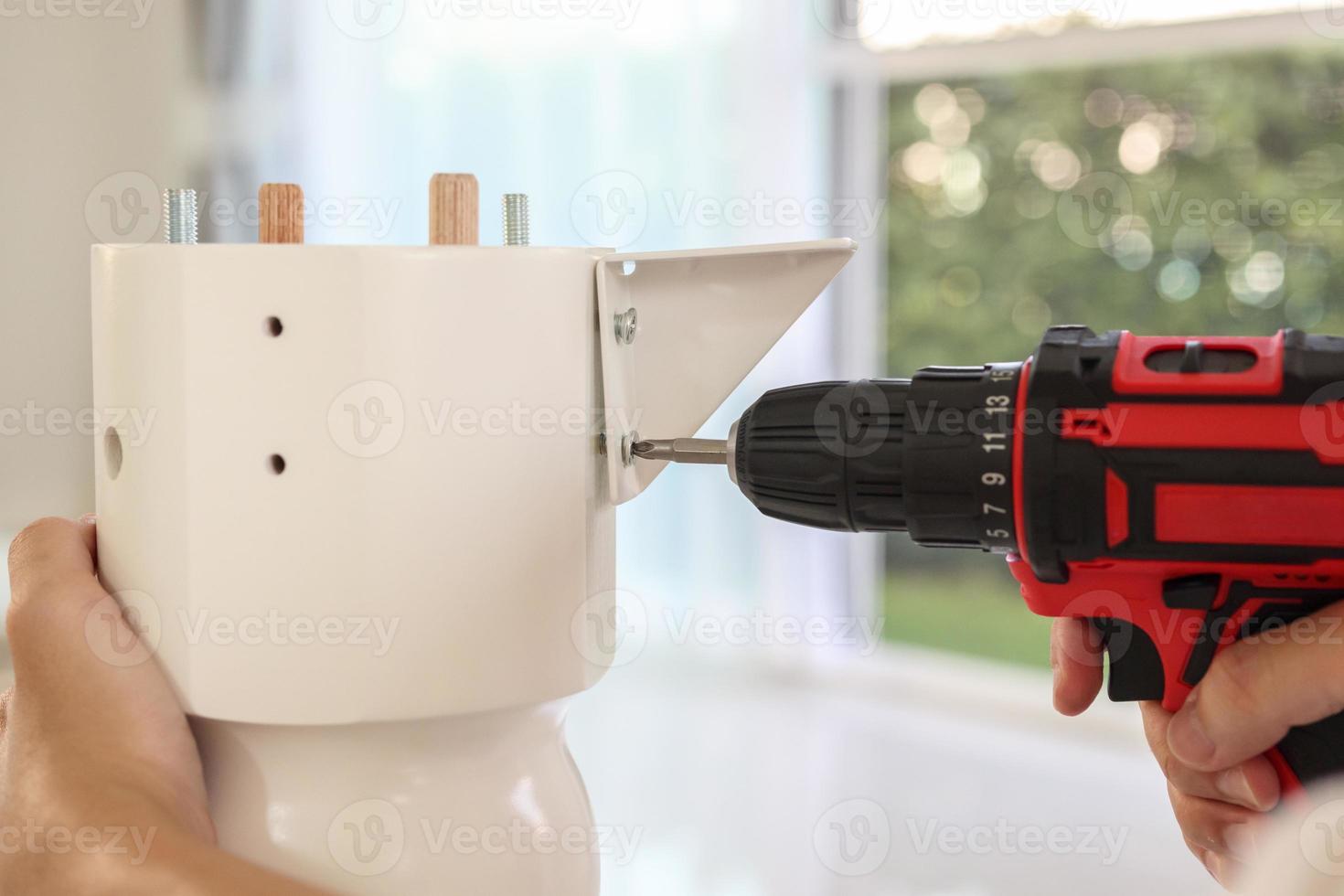 man assembling white table furniture at home using cordless screwdriver photo