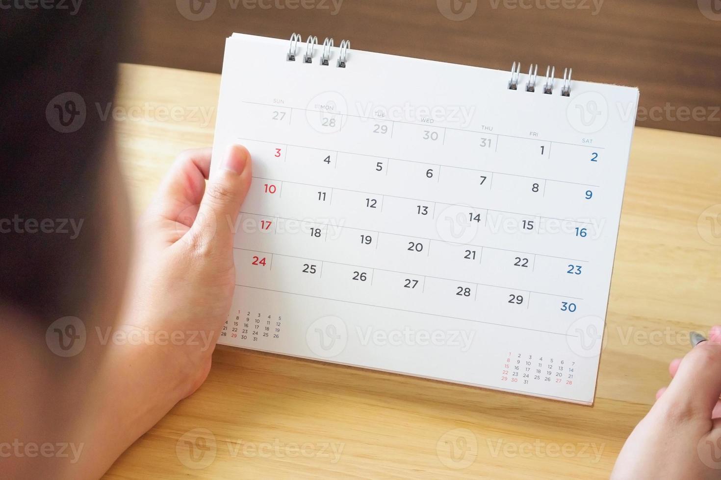 calendar page with female hand holding pen on desk table photo